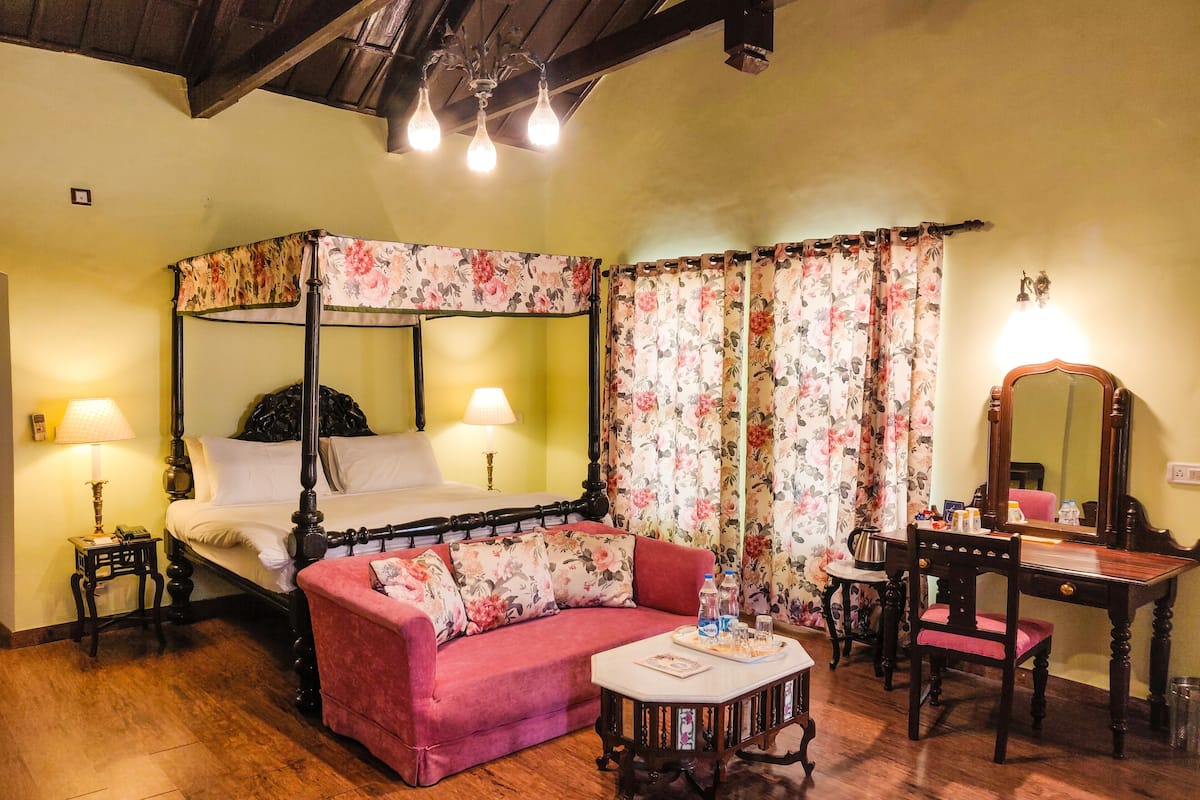 A four-poster bed with floral curtains, a pink sofa, a wooden desk, and a small table with a tray.