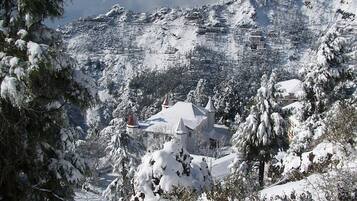 A snow-covered mountain landscape with a building featuring multiple towers and a snow-covered roof.