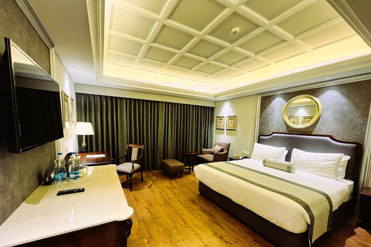 A hotel room with a large bed, a desk, a chair, a TV, and a mirror.