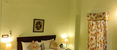 A bedroom with a wooden bed, two bedside lamps, a nightstand with a telephone, a framed picture on the wall, and a floral curtain.