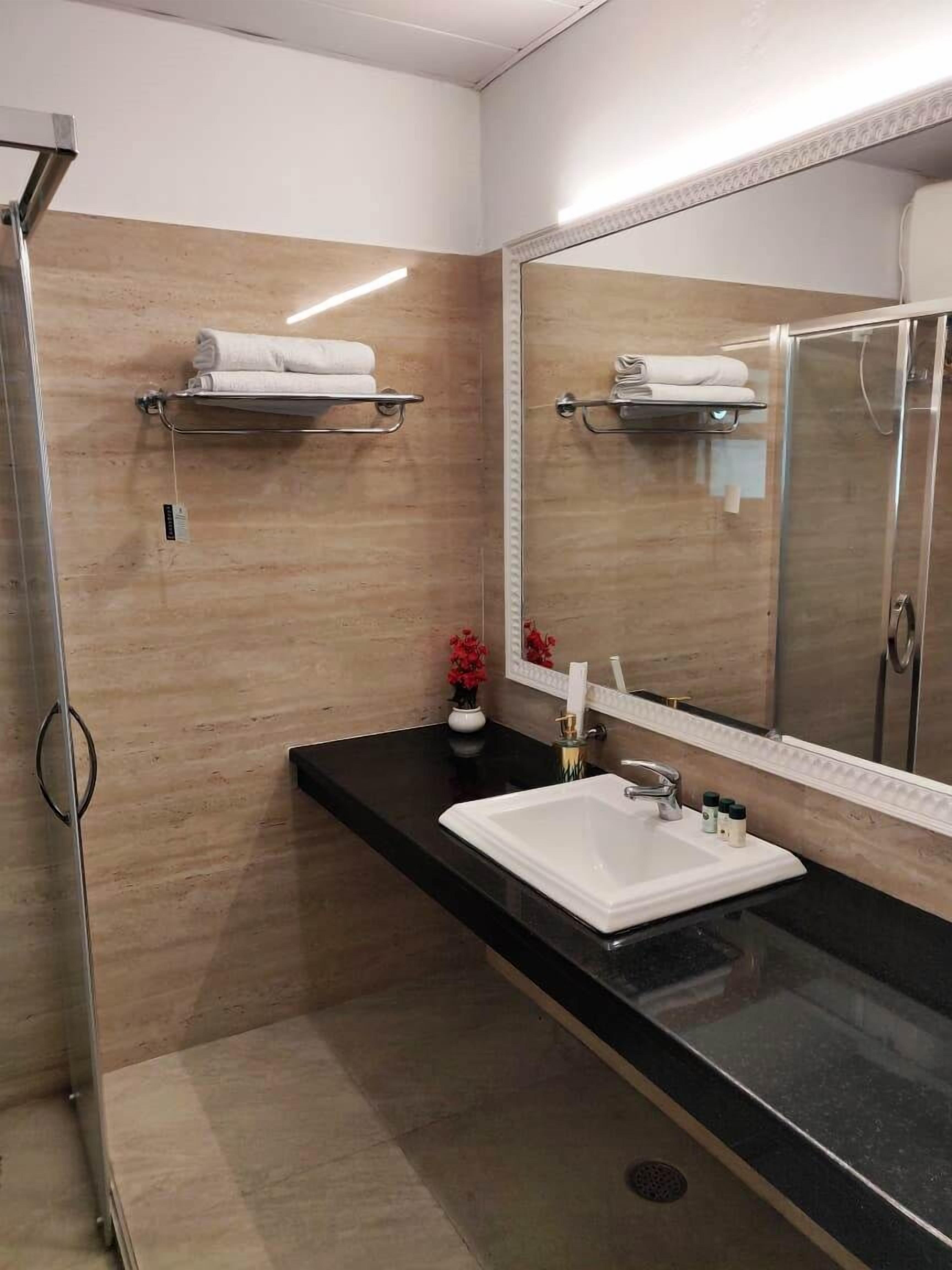A modern bathroom with a black countertop, a white sink, a large mirror, and a shower area.