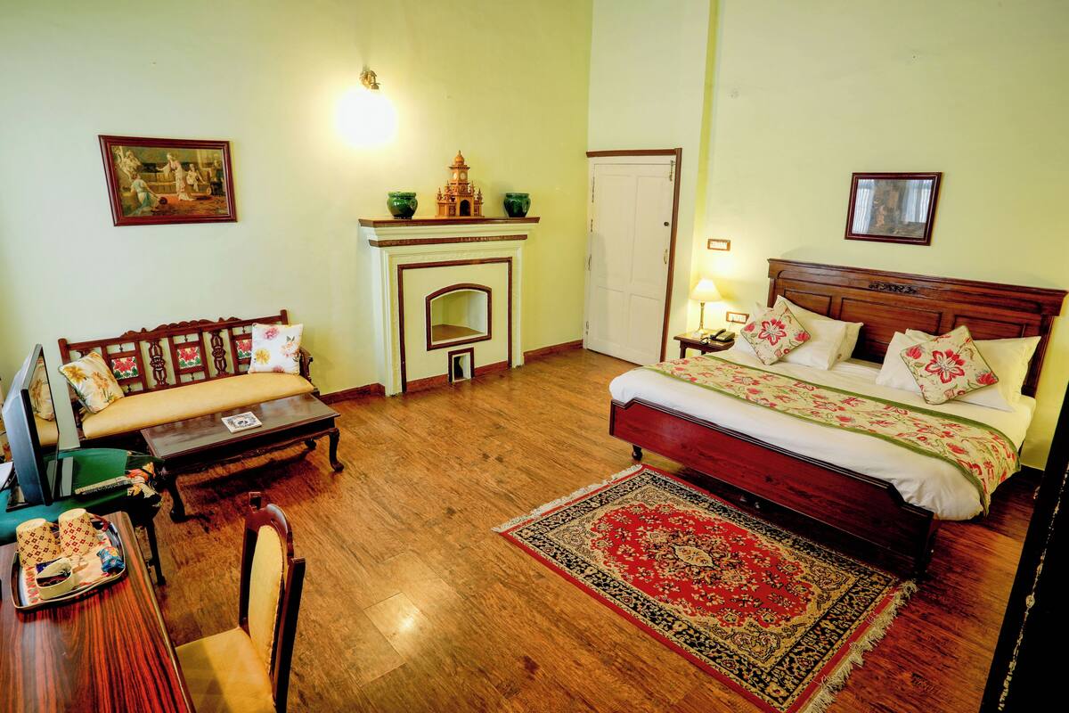 A bedroom with a bed, a sofa, a small table, a chair, a fireplace, and a rug.