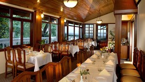 A restaurant with wooden interiors, large windows, and tables set for dining. - WelcomHeritage Kasmanda Palace (Mussoorie)
