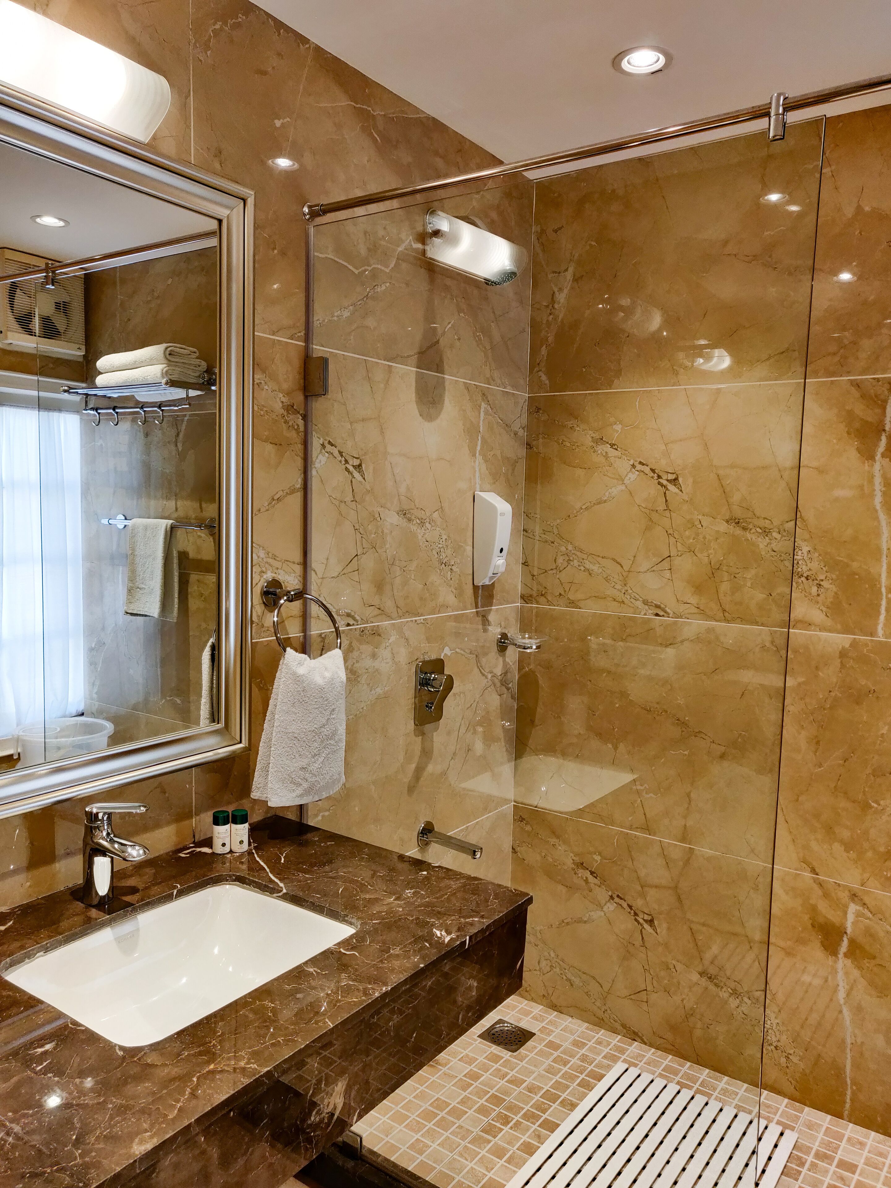 A modern bathroom with a marble vanity, a large mirror, a glass shower enclosure, and a towel rack.