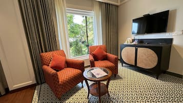 A hotel room with two patterned armchairs, a small round table, a television on the wall, and a patterned floor.