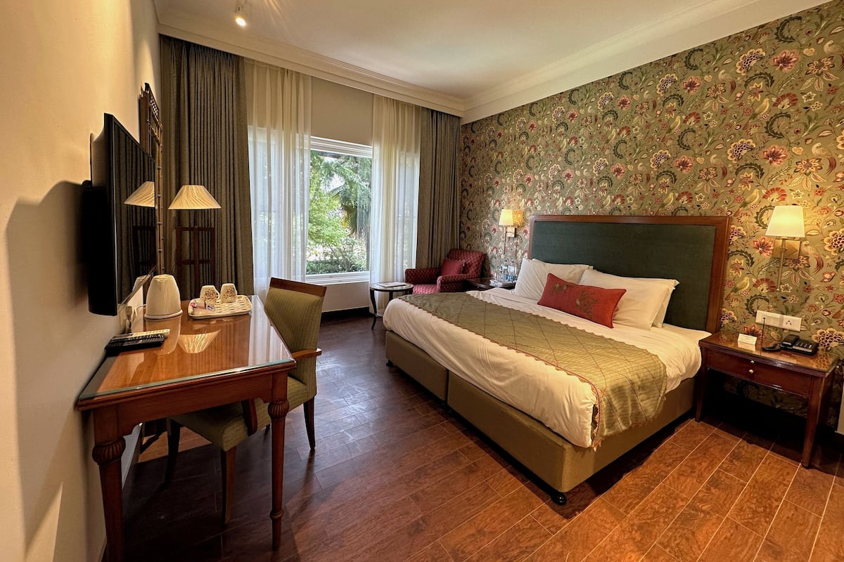 A hotel room with a bed, a desk with a chair, a television, and a window with curtains.