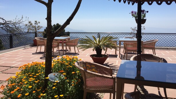 A terrace with wicker furniture, potted plants, and a view of the sea. - WelcomHeritage Kasmanda Palace (Mussoorie)