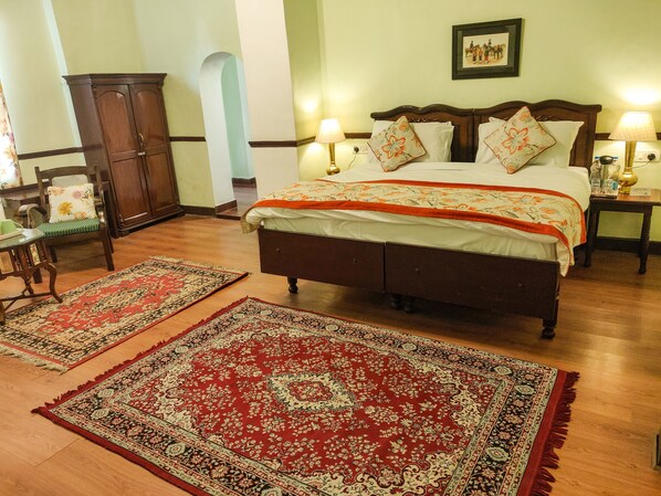 A bedroom with a large bed, two nightstands, a wooden wardrobe, and two patterned rugs on a wooden floor.