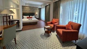 A hotel room with a bed, a desk, a chair, a sofa, a patterned carpet, and a ceiling fan. - WelcomHeritage Kasmanda Palace (Mussoorie)