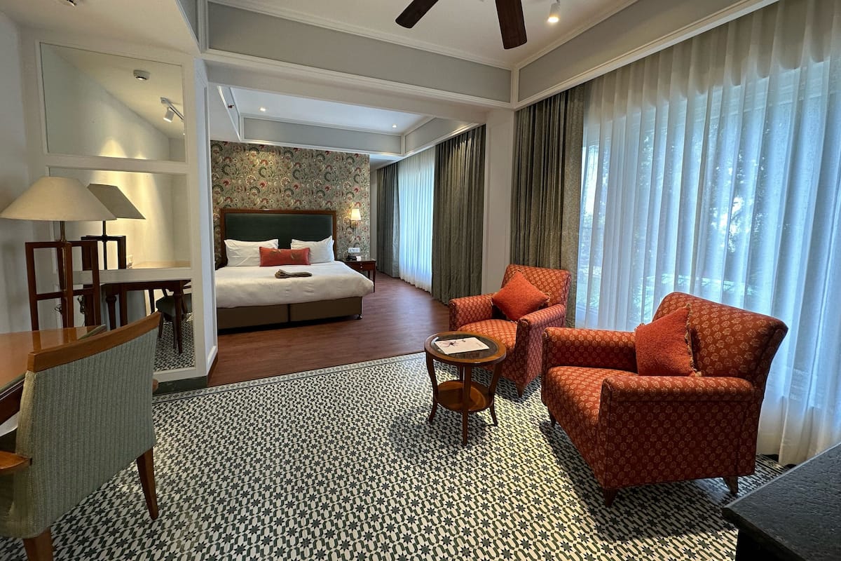 A hotel room with a bed, a desk, a chair, a sofa, a patterned carpet, and a ceiling fan.