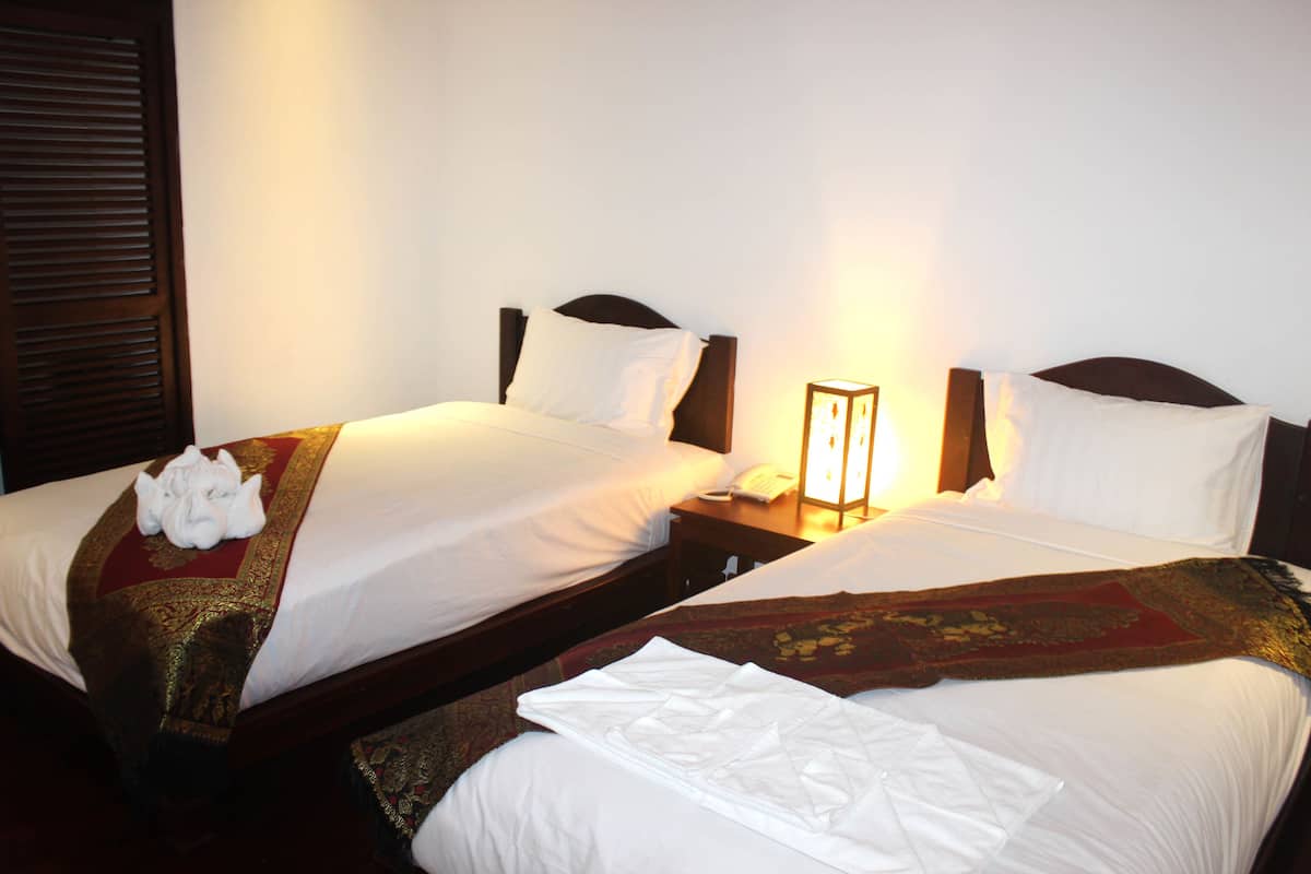 Two single beds with white linens, a wooden headboard, a nightstand with a lamp, and a wall-mounted phone.