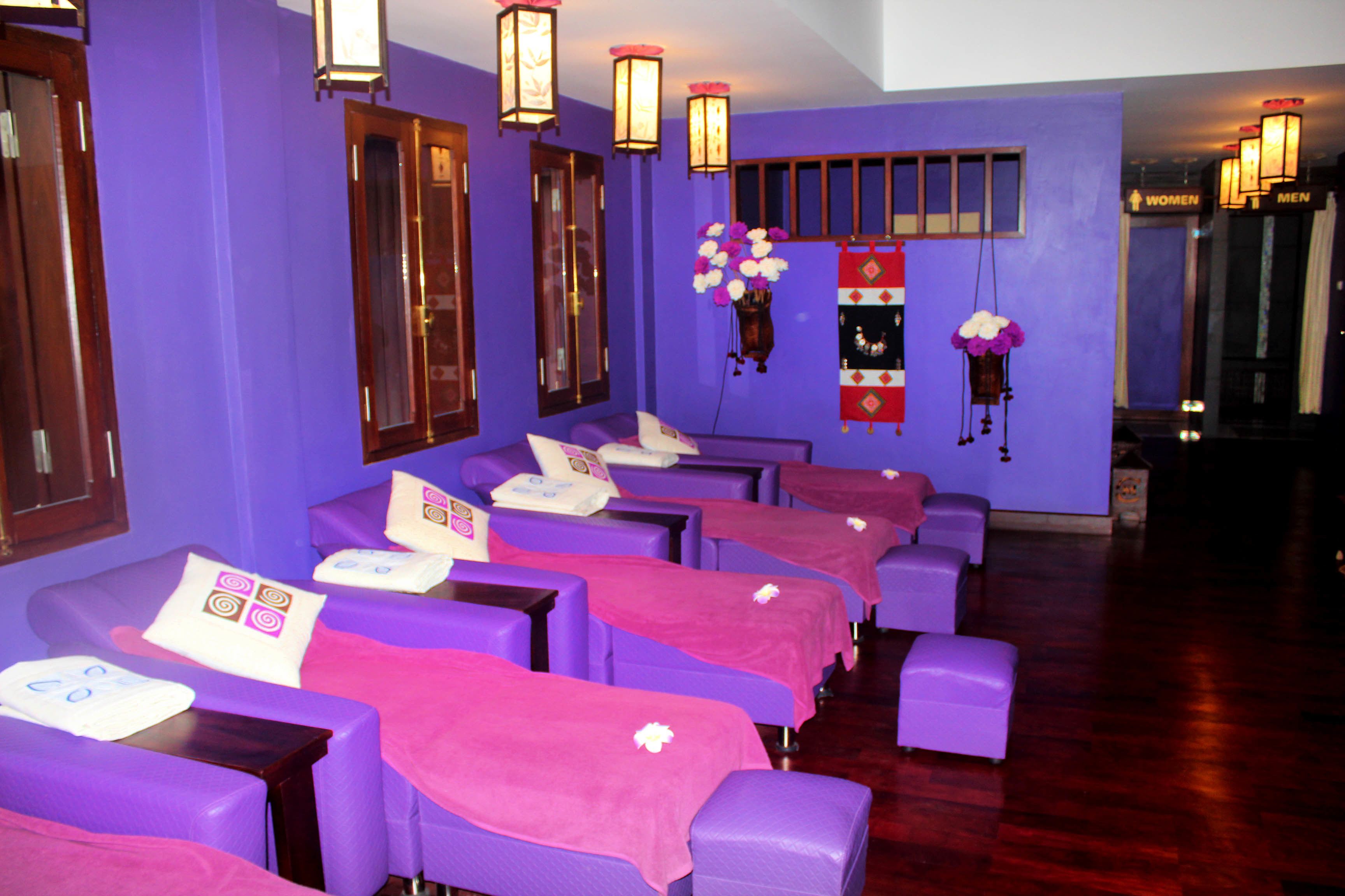 A room with purple walls, multiple massage tables with pink towels, and wooden doors.