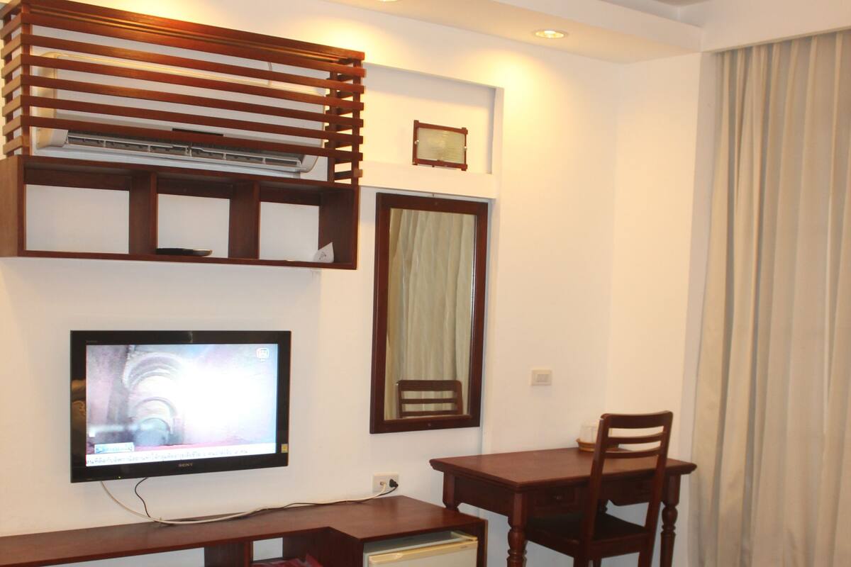 A hotel room with a bunk bed, a desk with a chair, a television, and a small refrigerator.