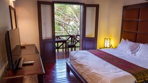 A hotel room with a large bed, a desk with a chair, a TV, and a window with a view of trees.