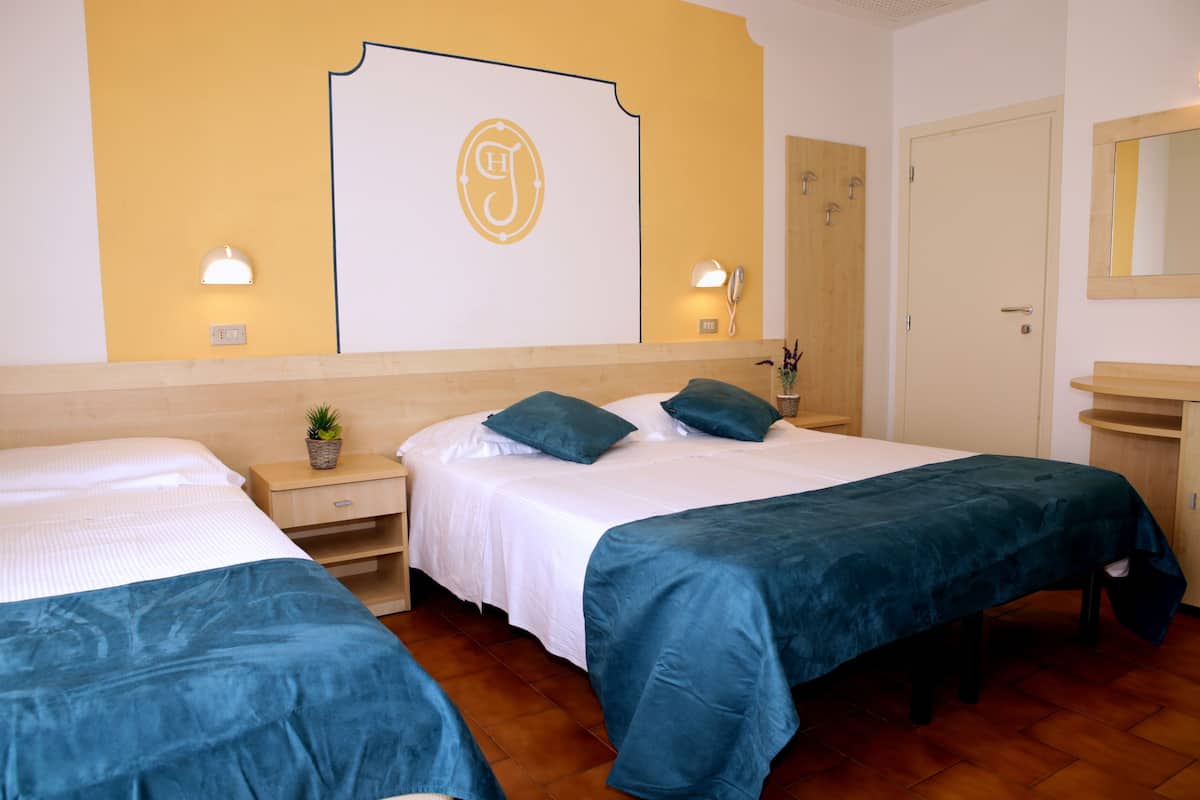 A hotel room with two single beds, a wooden headboard, a wall-mounted light fixture, a bedside table with a plant, and a wooden door.