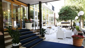 L’entrée d’un hôtel, avec un tapis bleu, un espace extérieur aménagé avec des sièges et des plantes en pot.