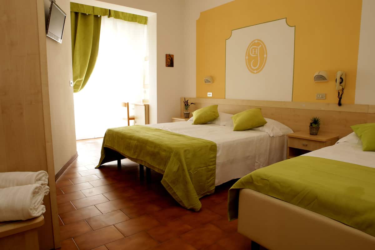 A hotel room with two beds, a small desk, a chair, a bedside table with a lamp, and a view of the outside.
