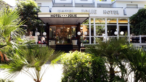 L’entrée d’un hôtel, avec un porche abrité, des plantes en pot et une façade blanche.