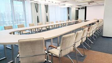 A conference room with a long table and chairs, large windows with curtains, and ceiling lights.