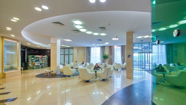 A spacious lobby with a curved ceiling, multiple seating areas, and a visible store named 'OPAH' on the left. - Hotel Victoria Minsk (Minsk)