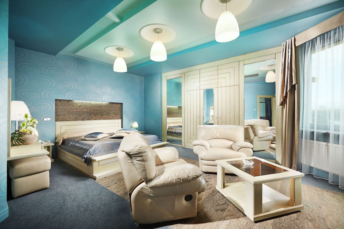 A modern hotel room with a large bed, a sofa, a chair, a coffee table, and a large mirror.