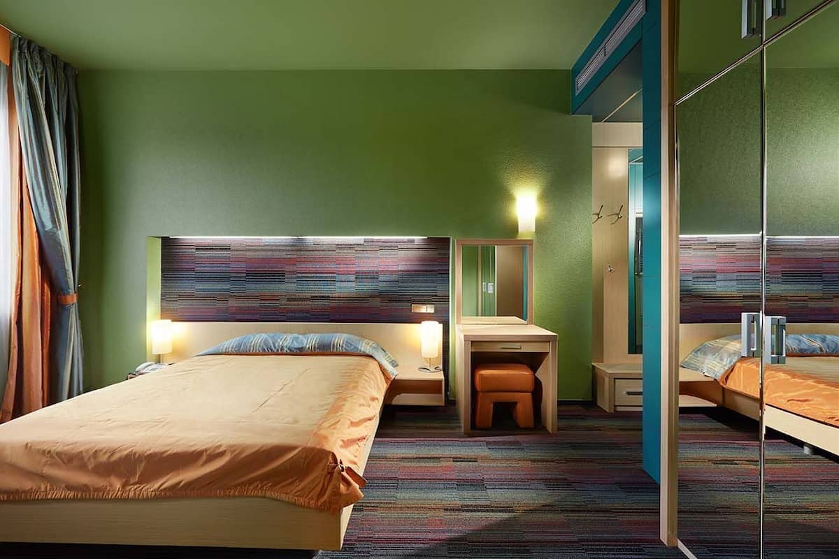 A hotel room with two beds, a desk, a mirror, and a small stool.