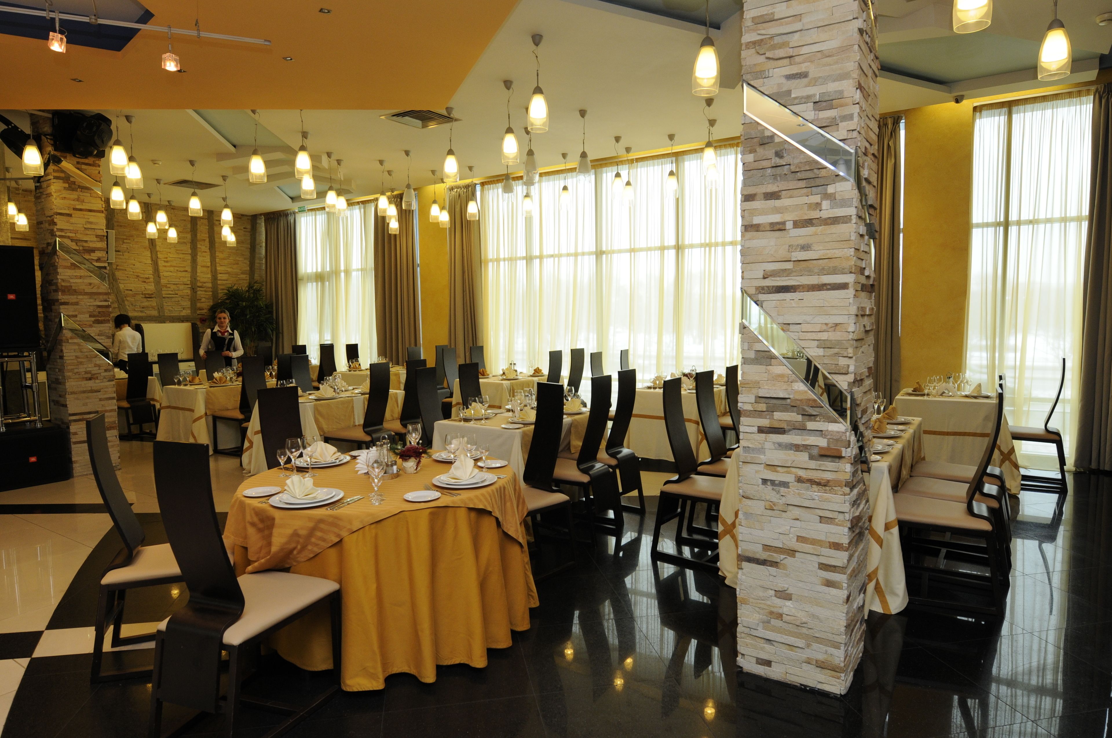 A spacious dining area with round tables, black chairs, and a stone accent wall.