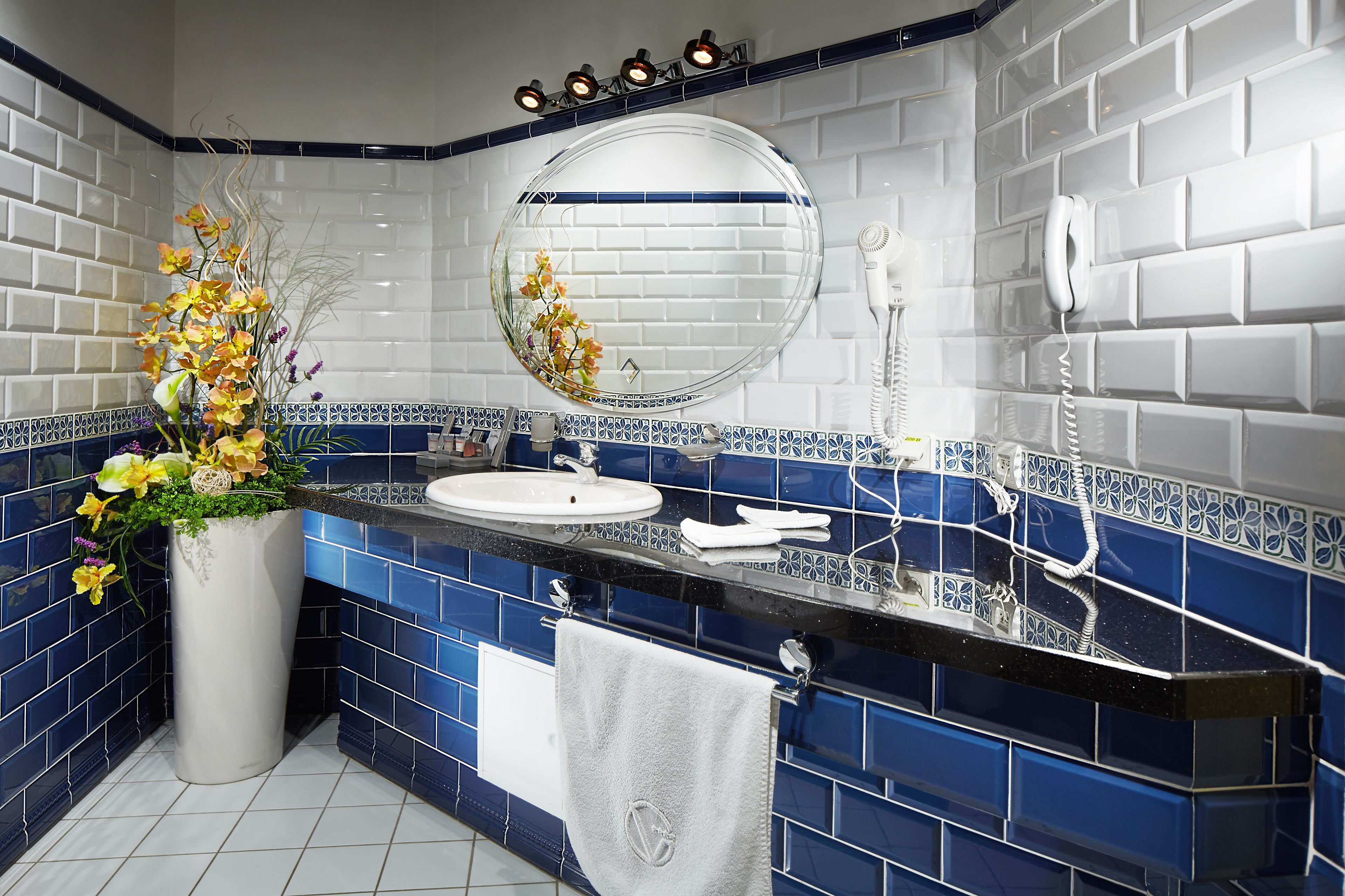 A bathroom with a white sink, blue tiles, a mirror, and a white towel hanging on the wall.