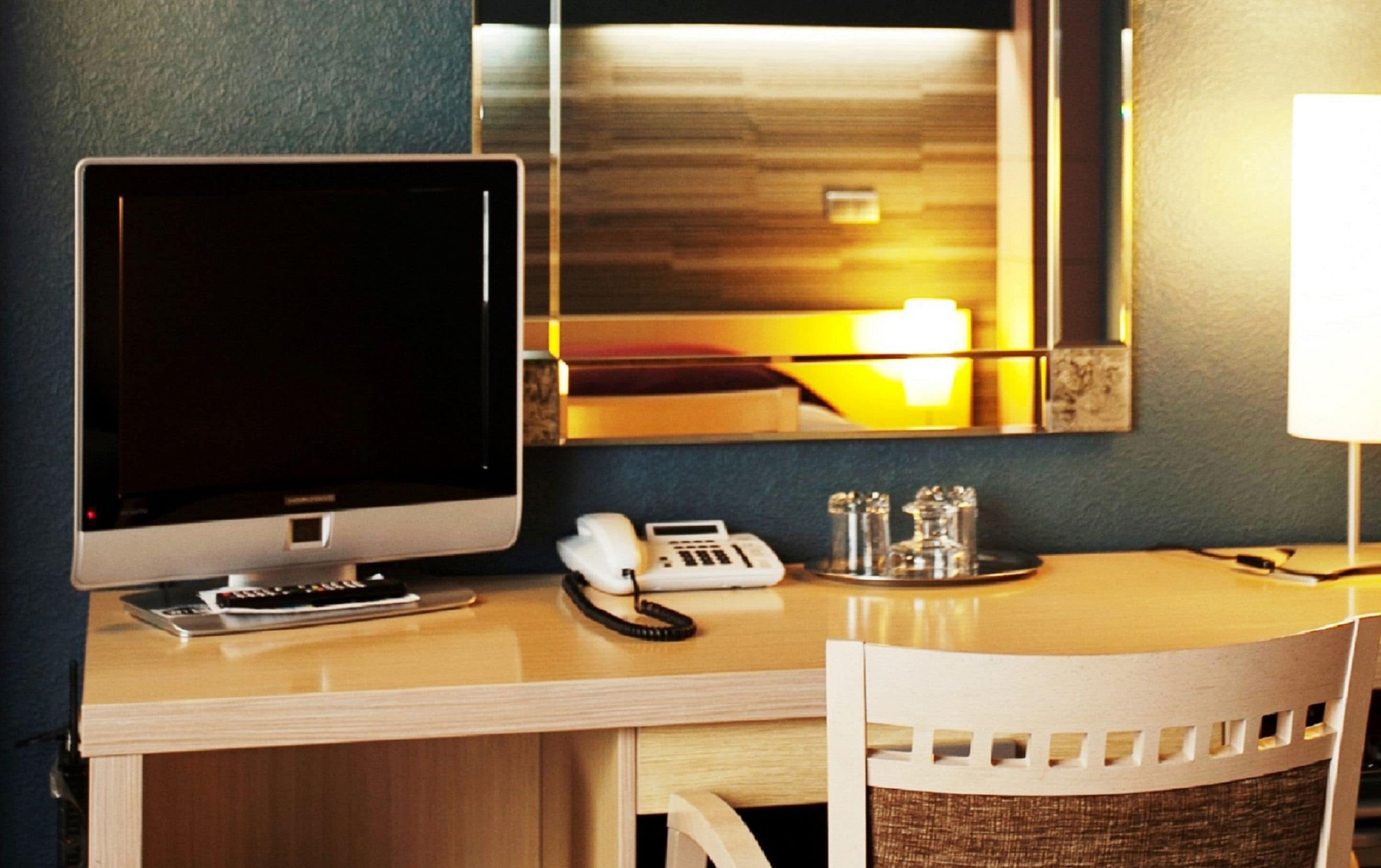 Ein Schreibtisch im Hotelzimmer mit Computerbildschirm, Telefon und Lampe.