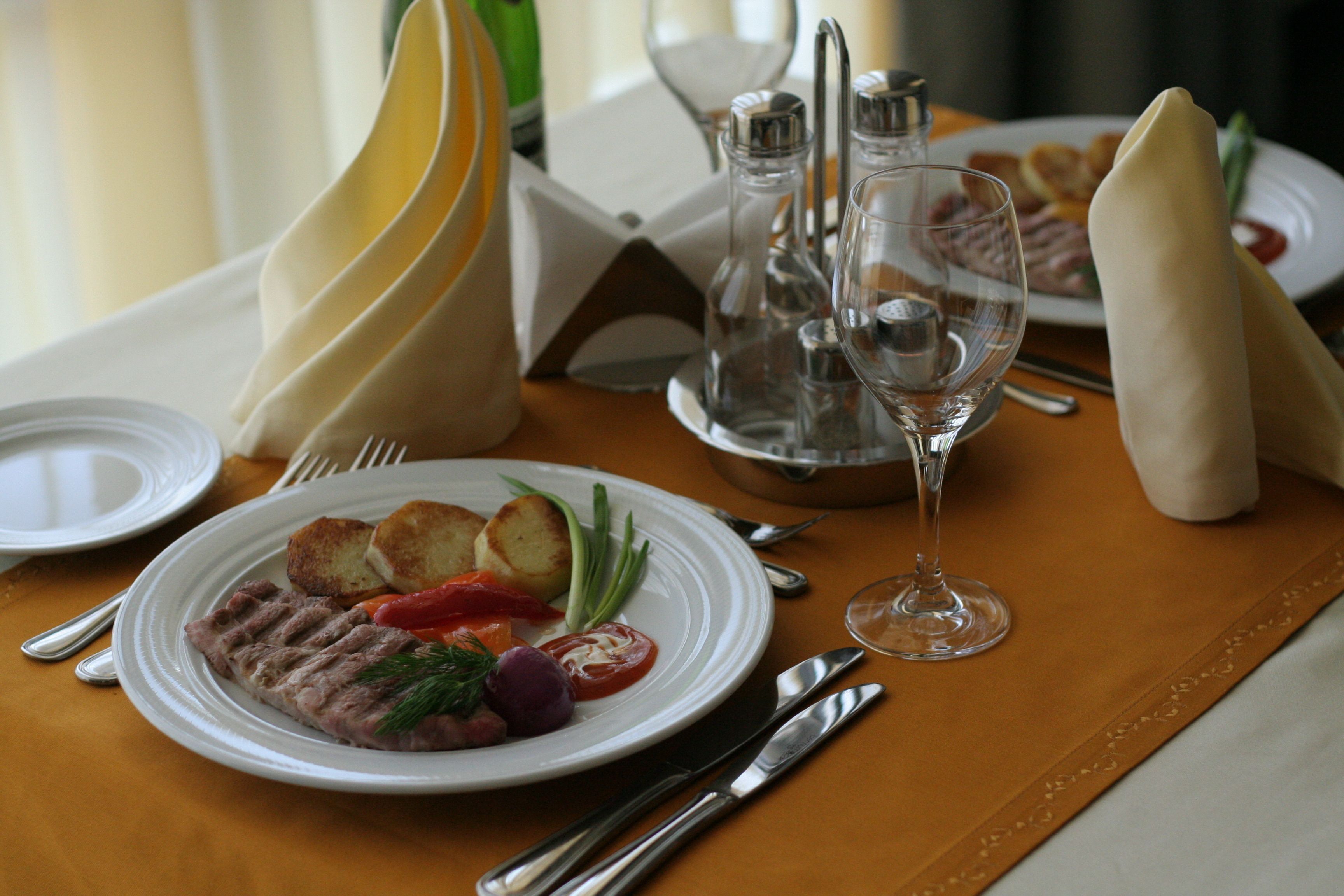 Mesa de comedor dispuesta con platos, cubiertos y copas, lo que sugiere un ambiente de comedor formal.