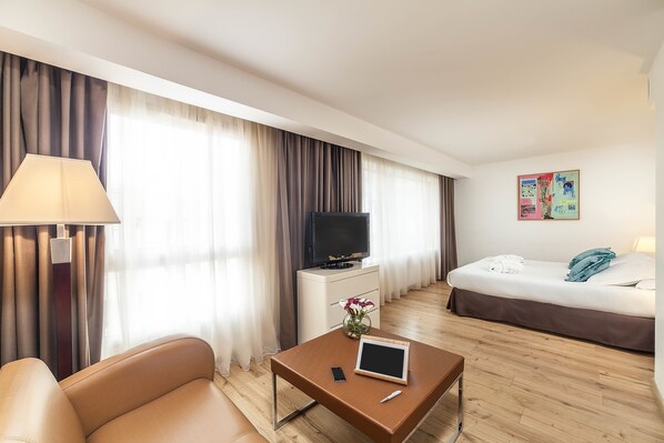 Una habitación de hotel con una cama, un televisor, un escritorio con lámpara y una mesita de centro.