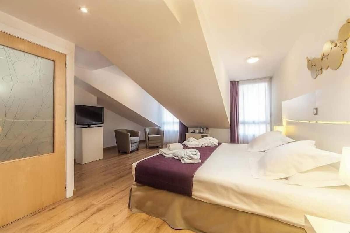 A hotel room with a bed, a TV, a desk, and a chair.