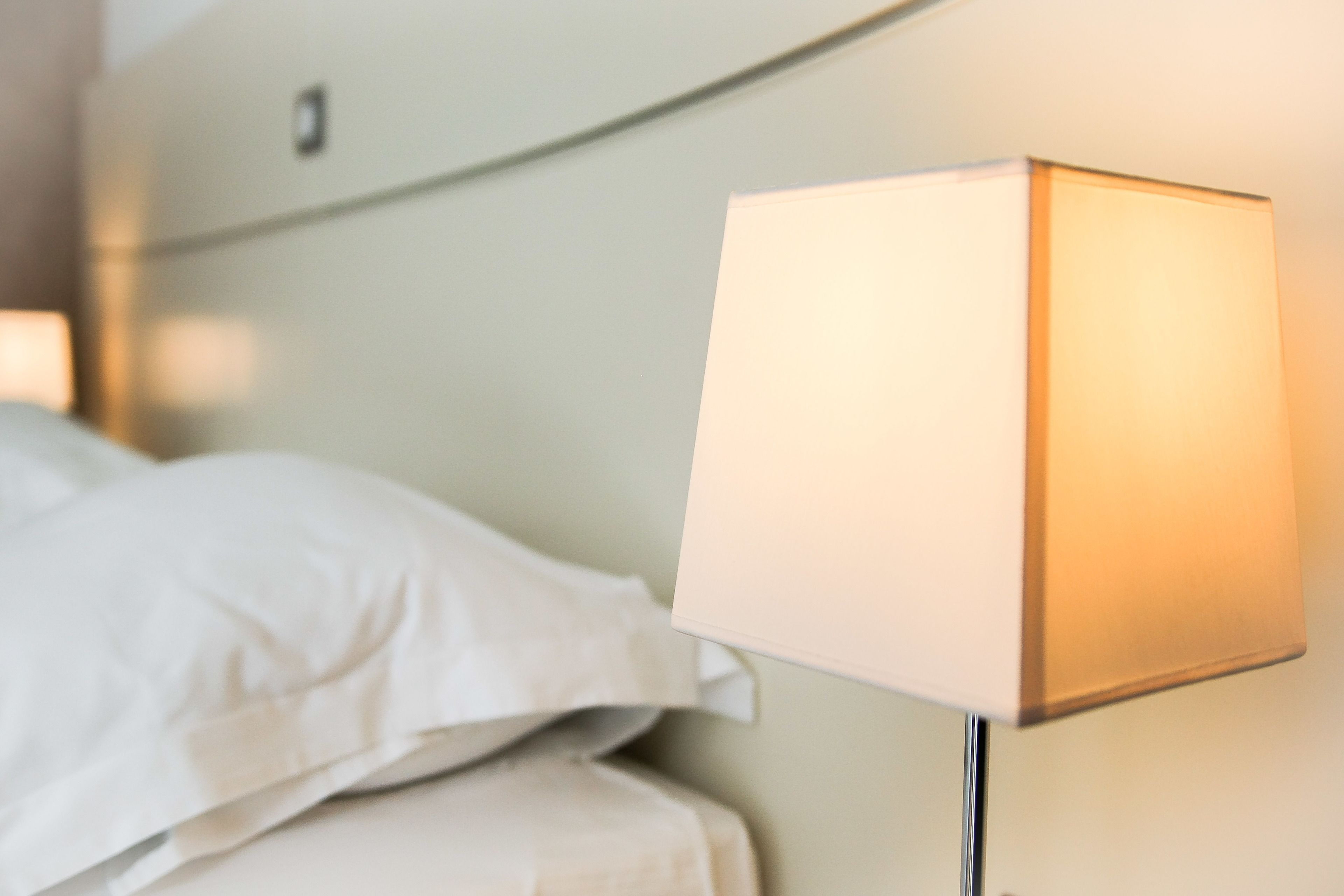 A bed with white linens and a bedside lamp with a white shade.