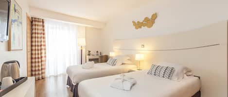 A hotel room with two beds, a desk, a chair, and a large window with curtains.