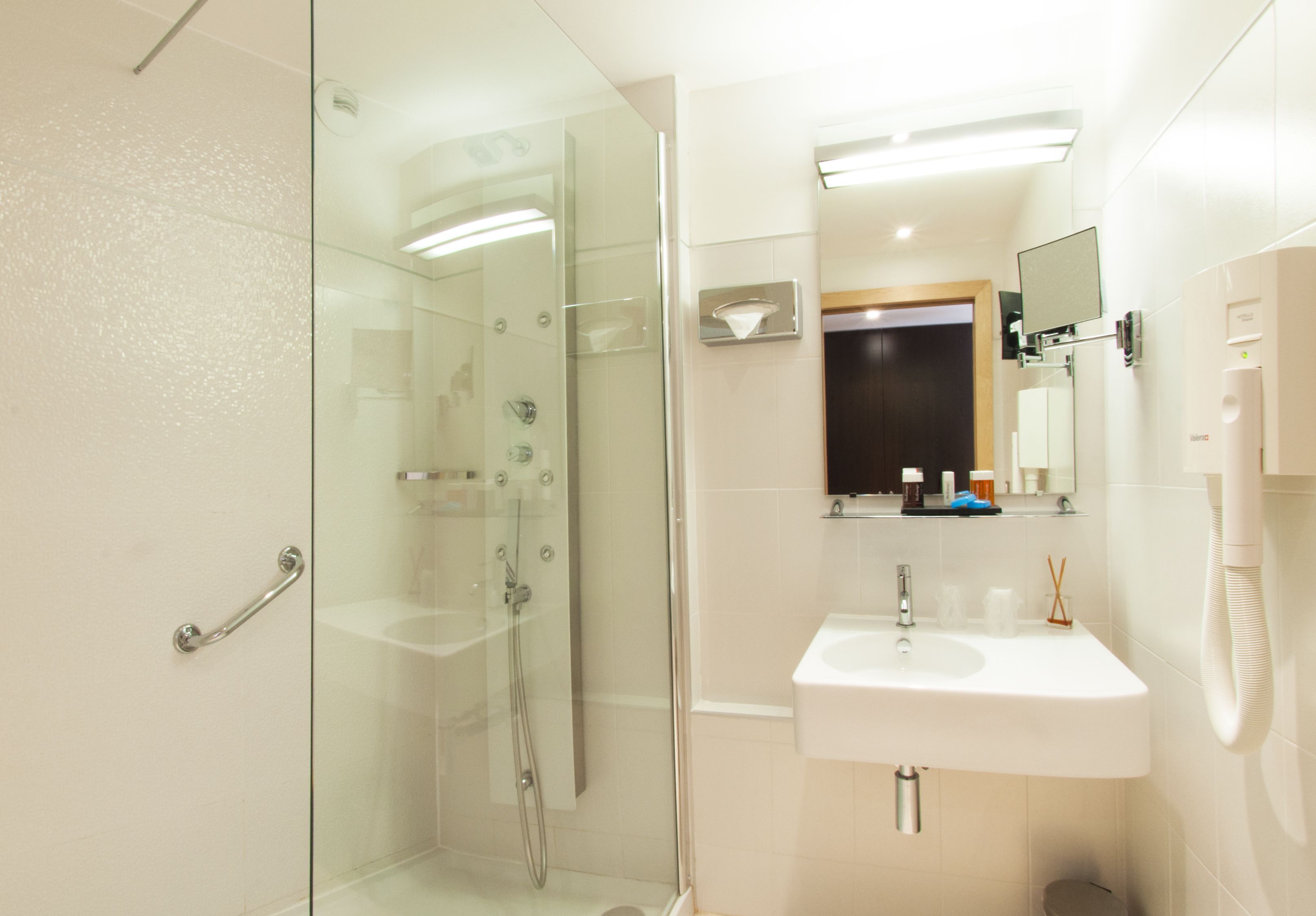 Un baño moderno con ducha envuelta en vidrio, un lavabo blanco y un espejo encima.
