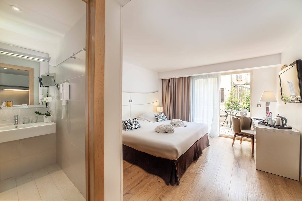 A hotel room with a bed, bedside table, desk, chair, and a view of the outside.