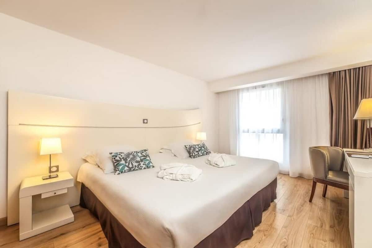 A hotel room with a large bed, bedside lamps, a desk, and a chair.