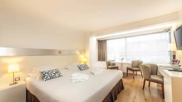 Una habitación de hotel con una cama grande, dos mesitas de noche con lámparas, un escritorio con silla y un televisor sobre el escritorio.