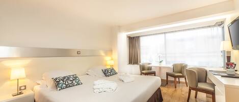 A hotel room with a large bed, two bedside tables with lamps, a desk with a chair, and a TV on the desk.