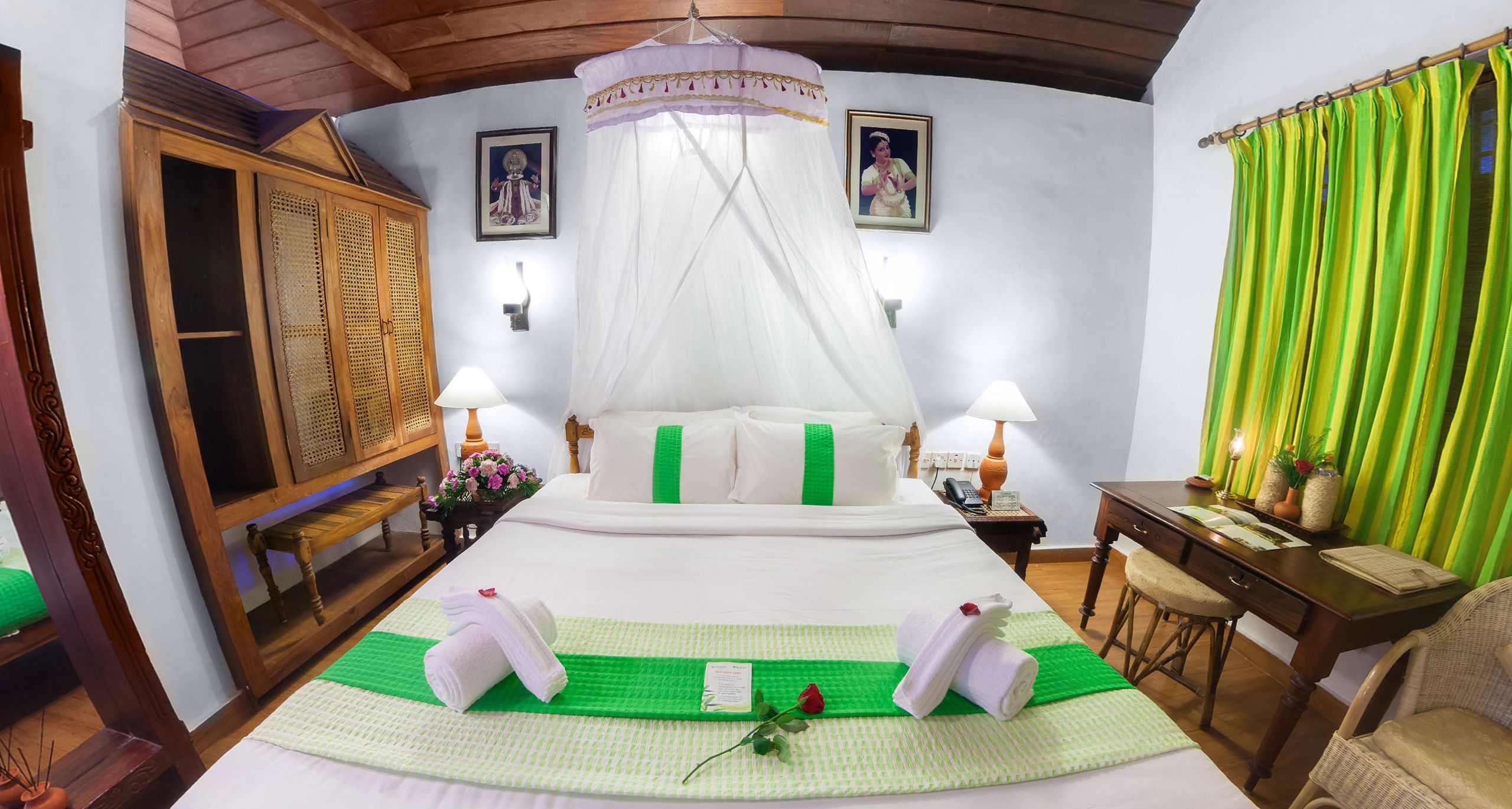A hotel room with a large bed, two bedside lamps, a wooden wardrobe, a desk with a chair, and a green curtain.