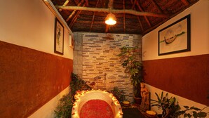 A room with a stone wall, a bathtub filled with water and flowers, and several potted plants. - Somatheeram Ayurveda Village (Neyyattinkara)