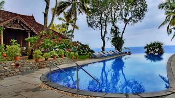 A swimming pool with a stone wall, lounge chairs, and tropical plants.