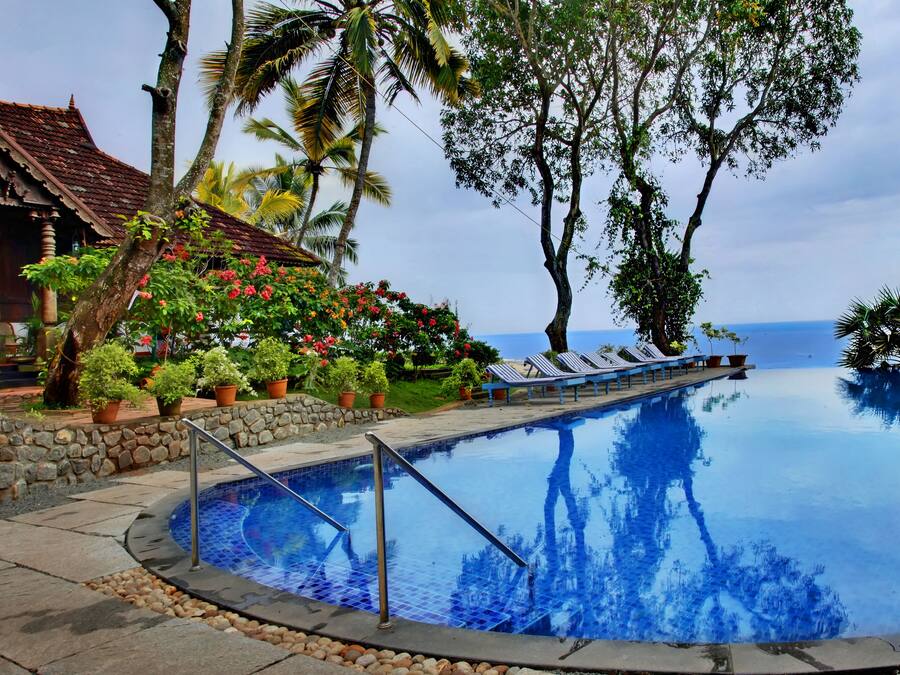 A swimming pool with a stone wall, lounge chairs, and tropical plants.