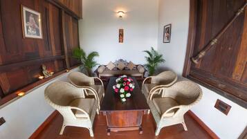 Um quarto com uma mesa de madeira e quatro cadeiras de vime, um sofá com almofadas e duas plantas em vasos.