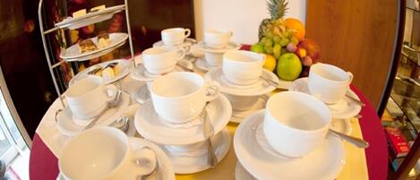 A breakfast setup with multiple white cups and saucers, a fruit bowl, and a three-tiered dessert stand.