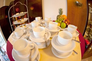 A breakfast setup with multiple white cups and saucers, a fruit bowl, and a three-tiered dessert stand. - Classic Hotel Kaarst (Kaarst)