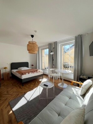 A modern bedroom with a bed, a sofa, a dining table, and a large window. - Classic Hotel Kaarst (Kaarst)