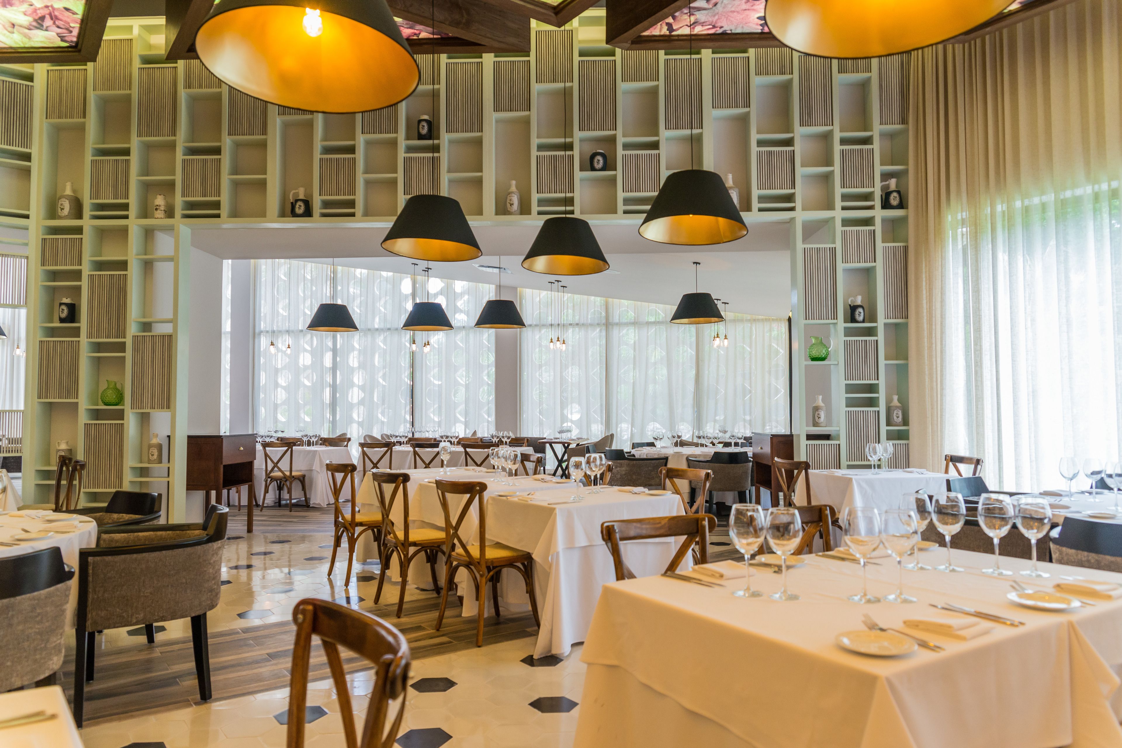 Un restaurante con varias mesas dispuestas para comer, con un interior moderno que incluye iluminación colgante y un diseño de pared con motivos.