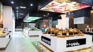 A modern restaurant interior with a central buffet area, a kitchen visible in the background, and a patterned floor. - Select Club at Sandos Playacar All Inclusive - Adults Only Area (Playa del Carmen)
