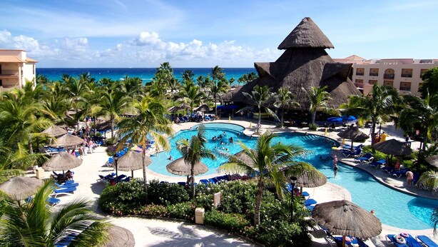 A resort with a large central pool, palm trees, and a thatched-roof structure. - Select Club at Sandos Playacar All Inclusive - Adults Only Area (Playa del Carmen)